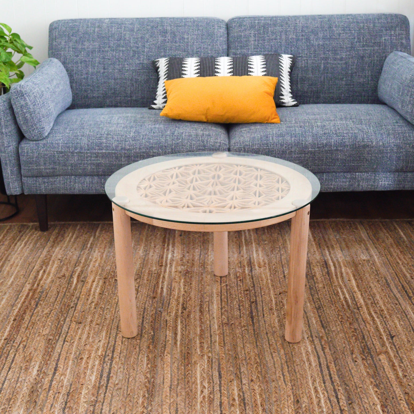 Kumiko Ripple Table is made with maple and basswood with a glass top. Displayed in a minimalist office with a grey couch.