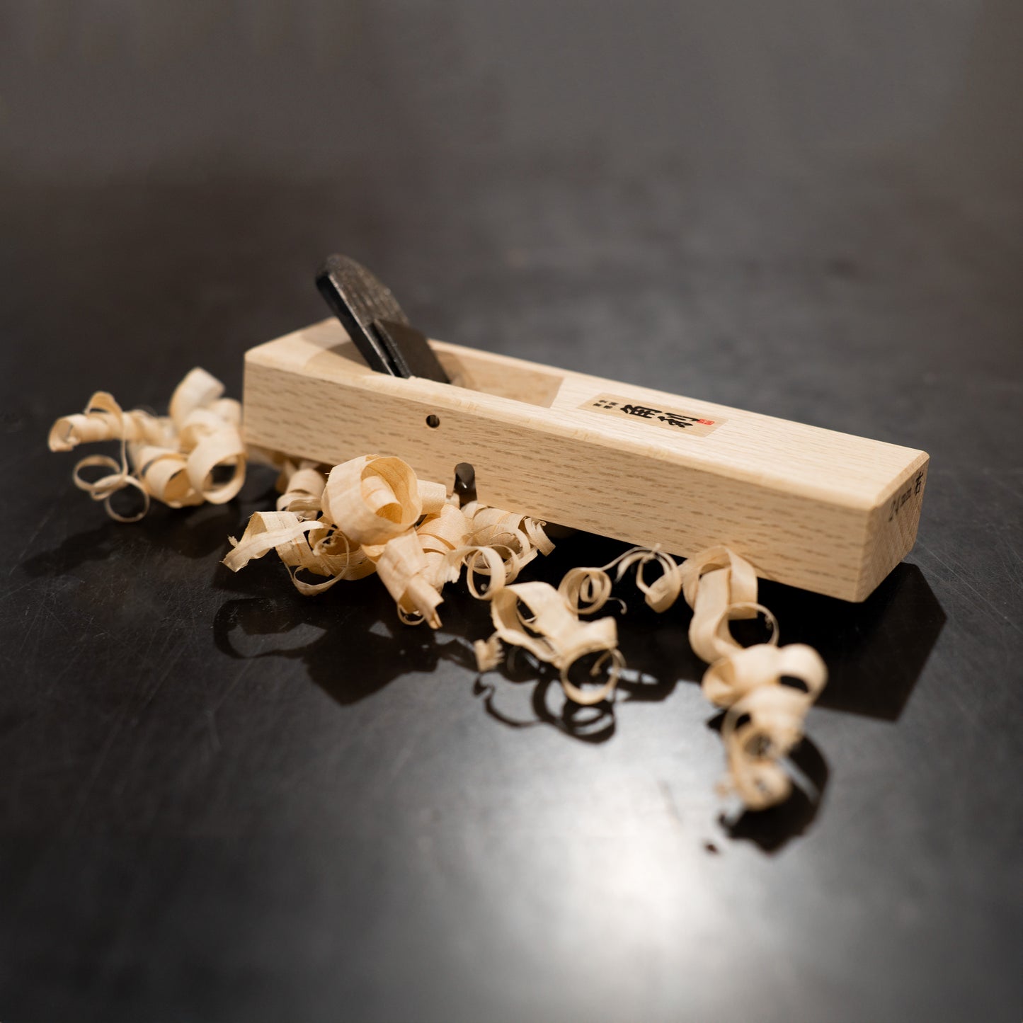 Kiwa Kanna (Hand Plane) - 24mm on a black background with wood shavings around it.