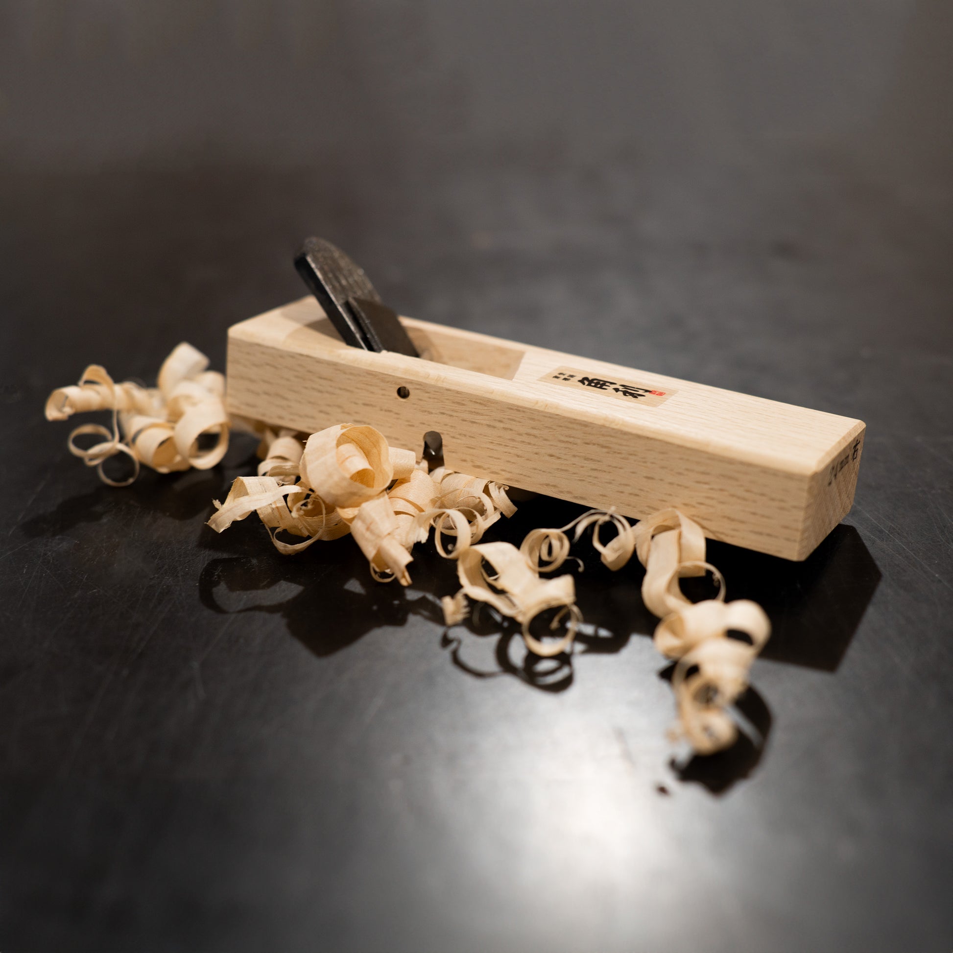 Kiwa Kanna (Hand Plane) - 24mm on a black background with wood shavings around it.
