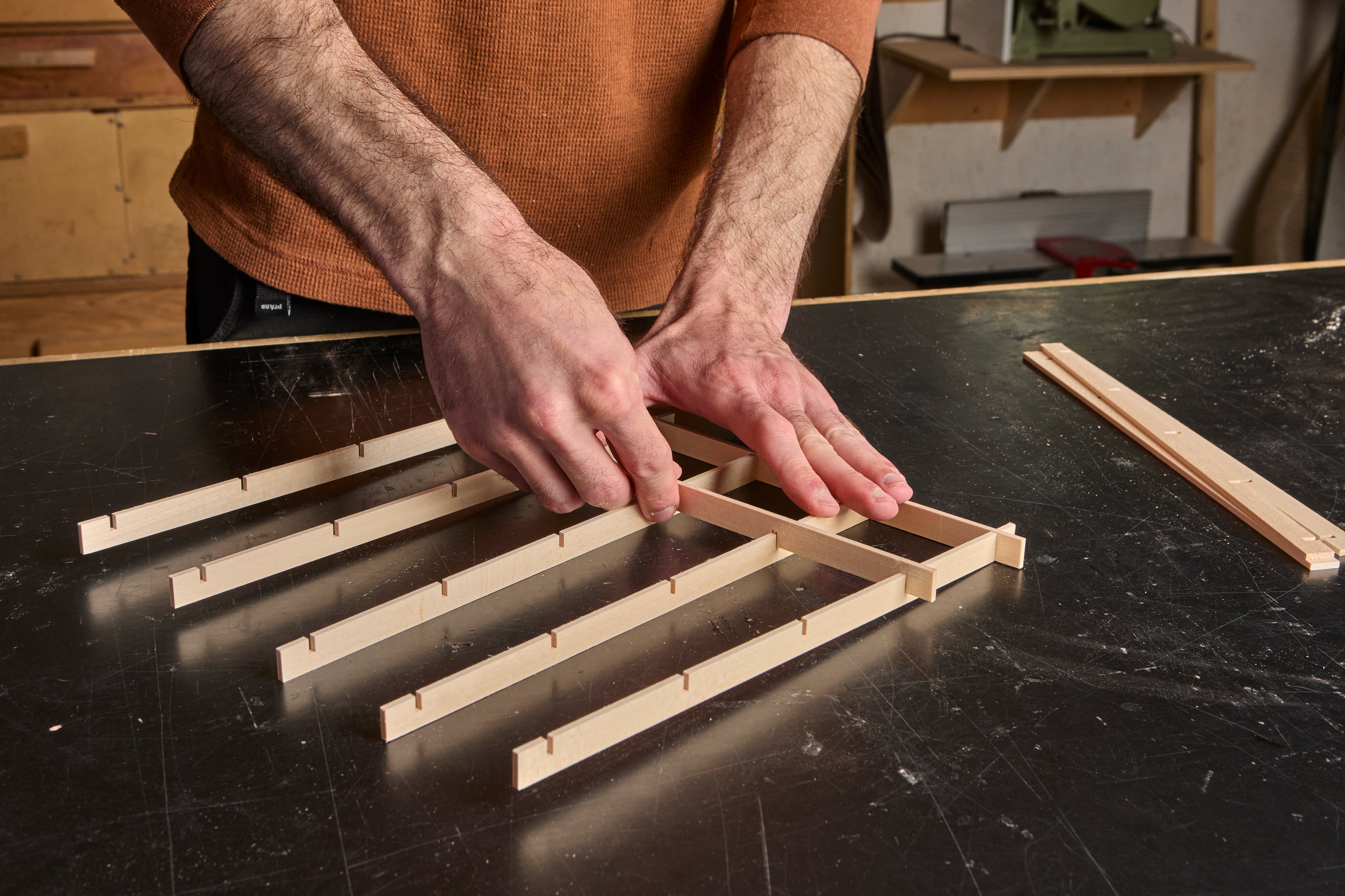 Johnny's hands putting together a kumiko grid on a black workbench tabletop.