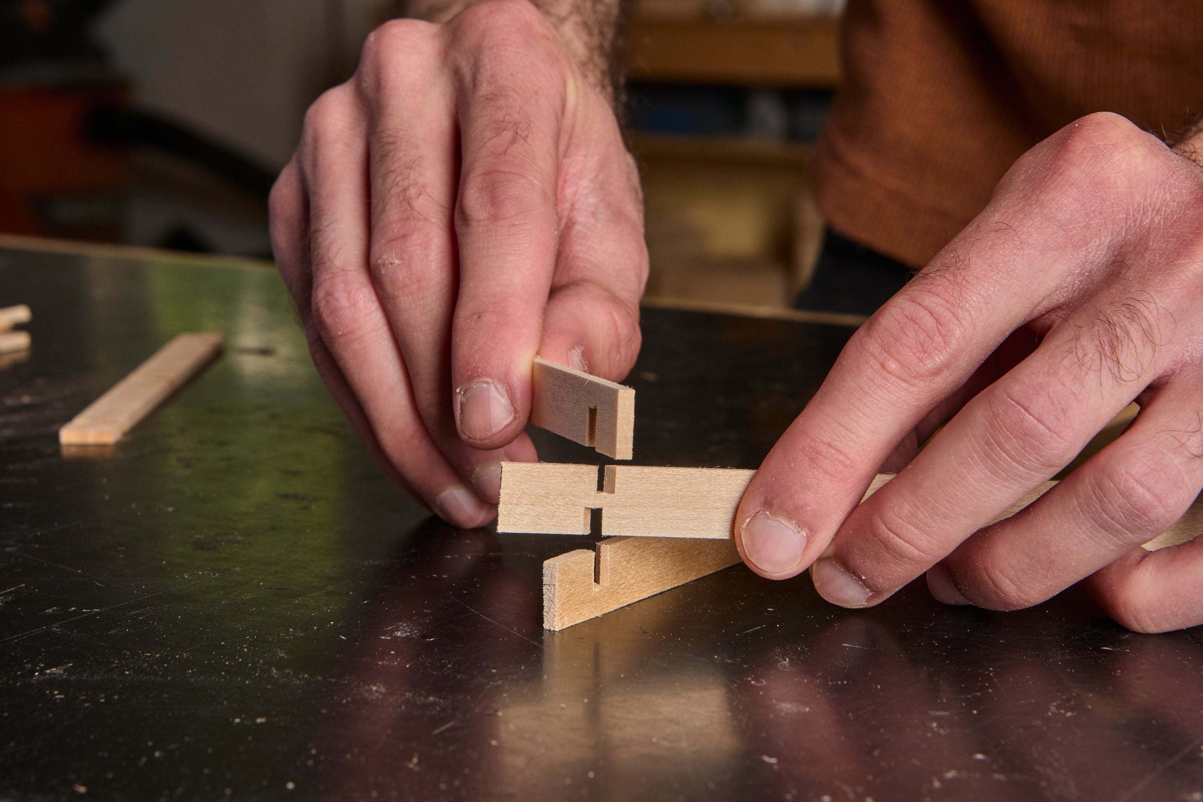 A closeup of Johnny's fingers putting together kumiko pieces on a black workbench tabletop.