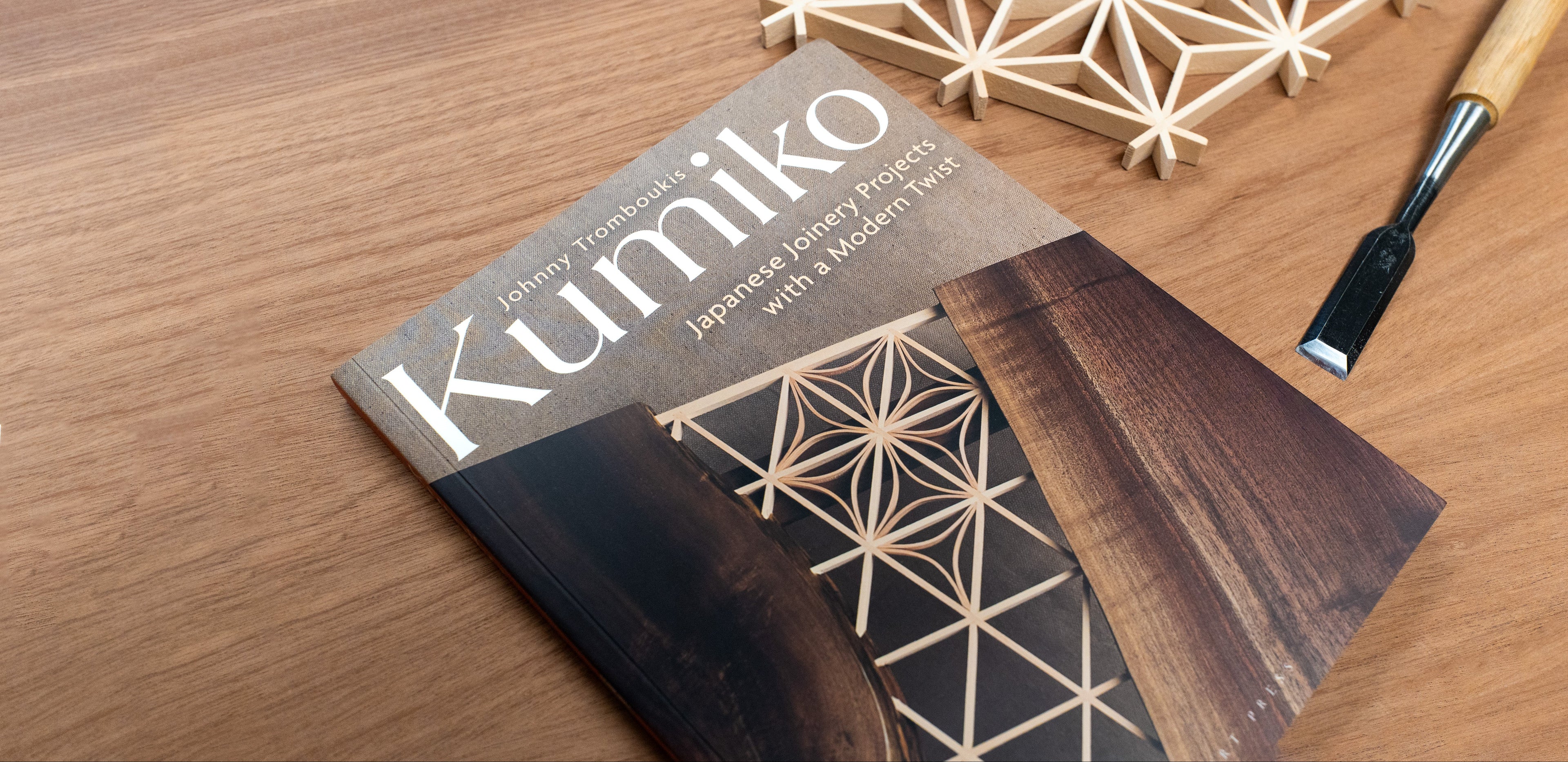 A book titled 'Kumiko Japanese Joinery Projects with a Modern Twist' lies on a wooden table, styled with a wooden chisel and geometric wooden joinery pieces.